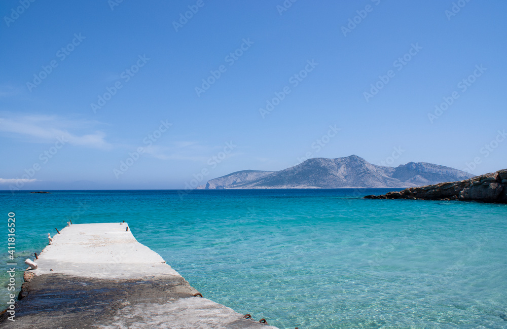 Koufonissi island Greece. Idyllic seascape. Crystal clear blue waters.  Summer landscape with small concrete jetty in foreground. View across the blue Aegean sea to the horizon.  Clear sky copy space.