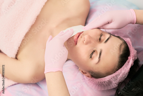 Professional beautician cleaning female face with cotton pad, caring for the face and body