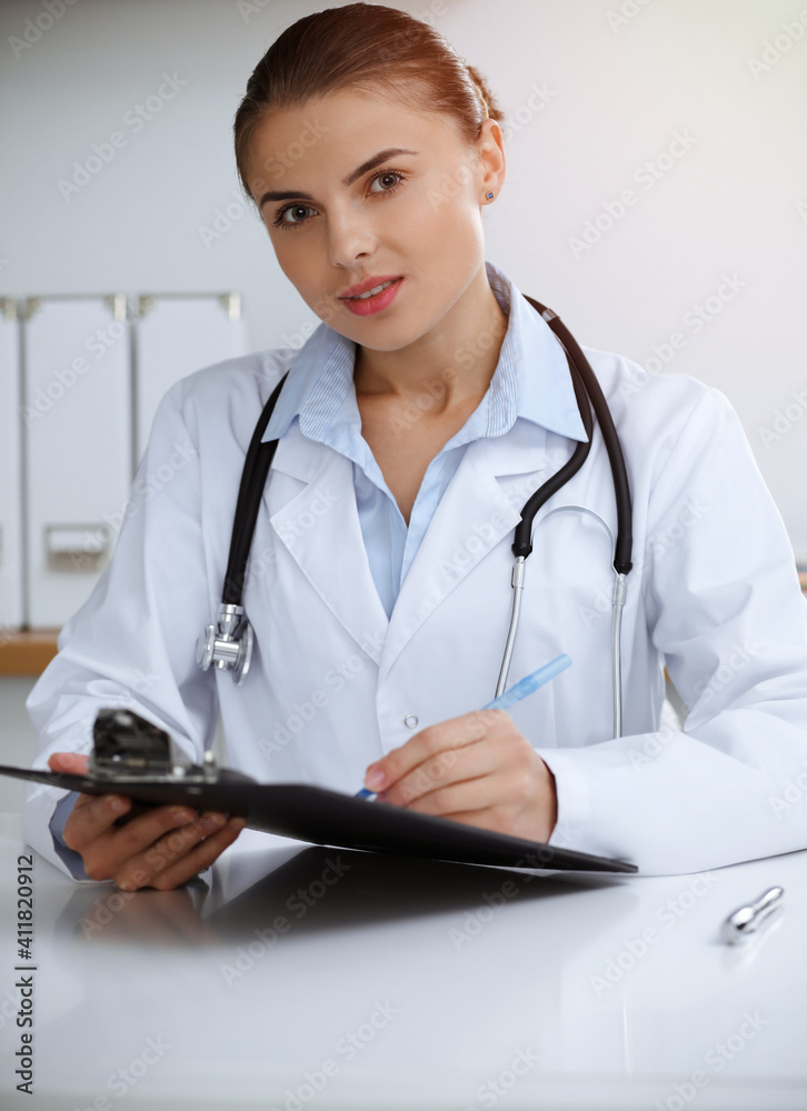 Woman-doctor sitting and working at clinic office. Portrait of female physician. Medicine concept Woman-doctor sitting and working at clinic office. Portrait of female physician. Medicine concept