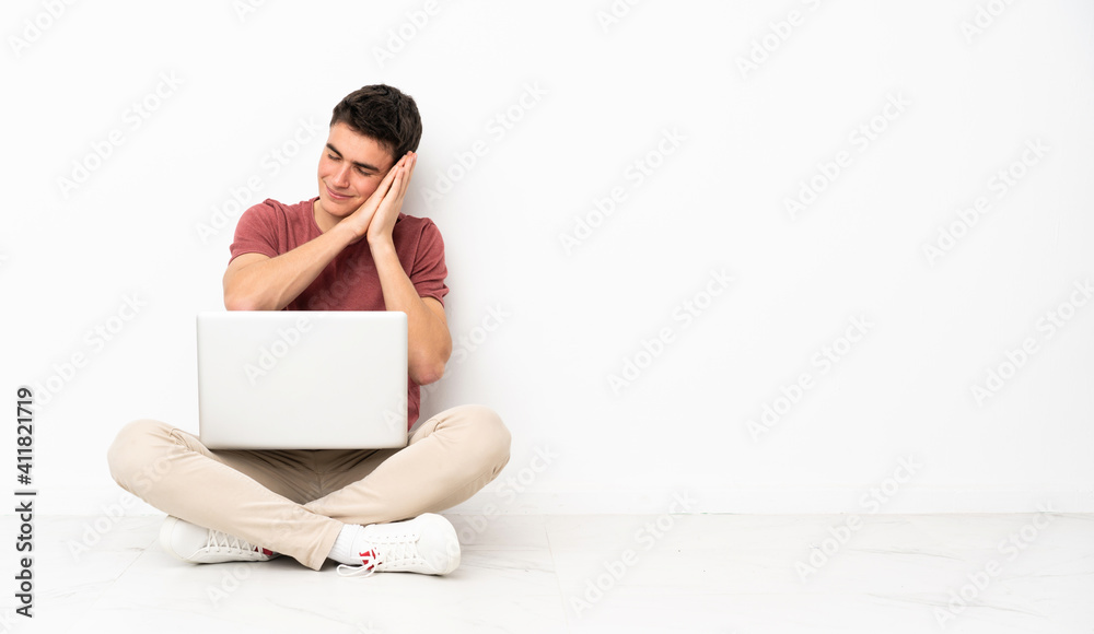 Teenager man sitting on the flor with his laptop making sleep gesture in dorable expression Teenager man sitting on the flor with his laptop making sleep gesture in dorable expression