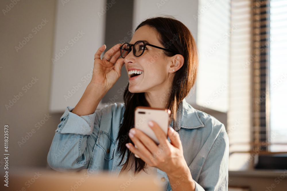 Happy charming woman using smartphone while working with laptop Happy charming woman using smartphone while working with laptop