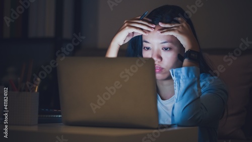 Asian woman student or businesswoman work late at night. Concentrated and feel sleepy at the desk in dark room with laptop or notebook.Concept of people work hard and burnout syndrome.