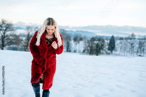 Frau im Schnee mit rotem Mantel lacht blonde lockige Haare Freude Winterlandschaft stapft durch den Schnee