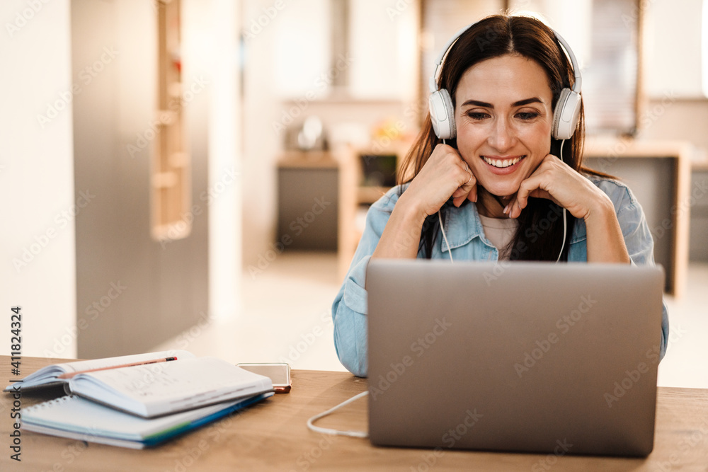 Happy beautiful woman in headphones smiling while using laptop