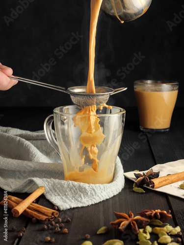 Bild auf Leinwand Masala tea is poured through a sieve into a glass mug