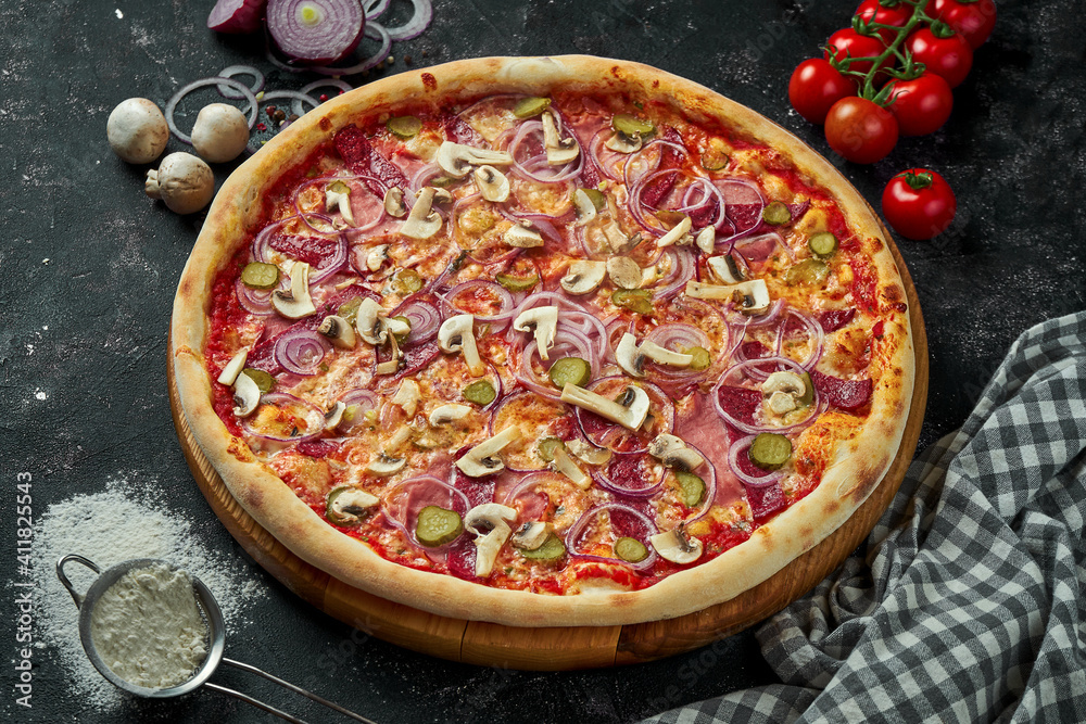 Oven-baked Italian pizza with red sauce, cheese, salami, ham and mushrooms in a composition with ingredients on a dark background. Close up