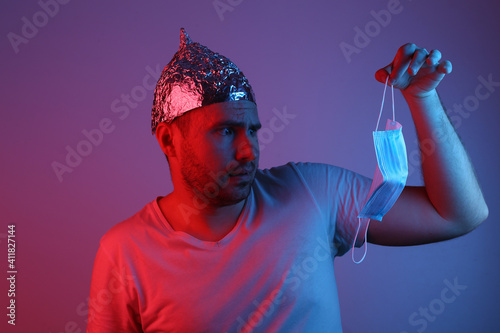 Fotografía Bearded Man in foil hat holding medical mask in blue red neon light