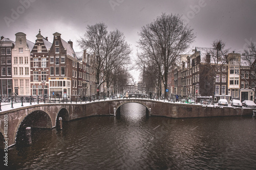 Winter snow view of Dutch canal and old houses in the historic city of Amsterdam, the Netherlands