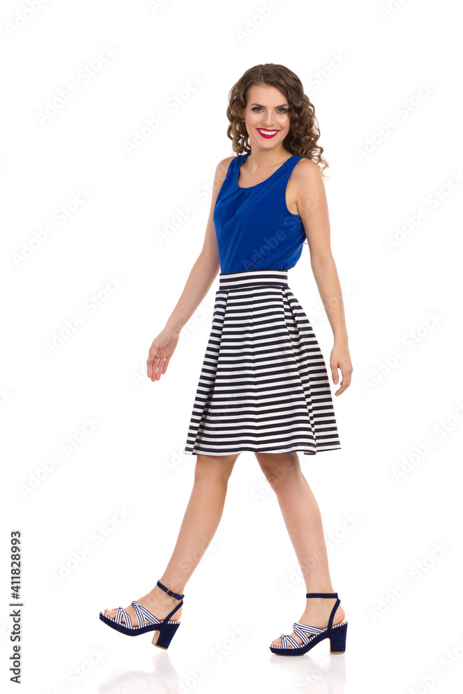 Side View Of Walking Smiling Young Woman In Striped Skirt And High Heels. Side View Of Walking Smiling Young Woman In Striped Skirt And High Heels.