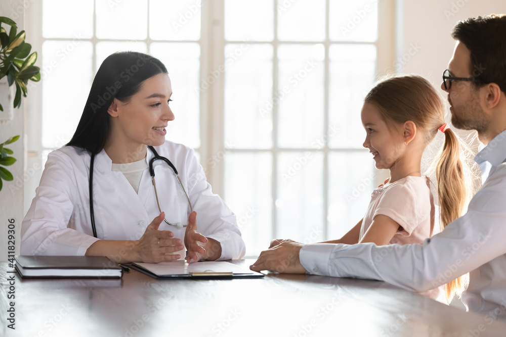 Young Caucasian female doctor in white uniform consult little girl patient visit hospital with father. Woman pediatrician examine small child at consultation in clinic with dad. Healthcare concept. Young Caucasian female doctor in white uniform consult little girl patient visit hospital with father. Woman pediatrician examine small child at consultation in clinic with dad. Healthcare concept.