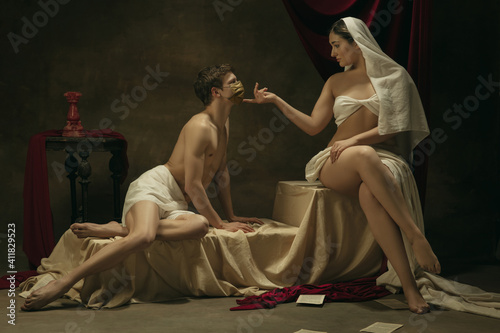 No kisses with golden face mask. Modern remake of classical artwork with coronavirus theme - young medieval couple on dark background, golden colored. Concept of coronavirus, pandemic, creativity. photo