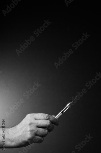 Black and white image of man's hand holding syringe upwards in fingertips with dramatic lighting and text space above