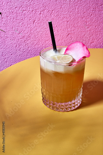 drink z limonką i płatkiem róży na żółto różowym tle. podany z ozdobną rurką. 