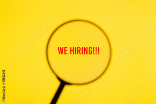 Text we hiring on yellow screen through magnifying glass.