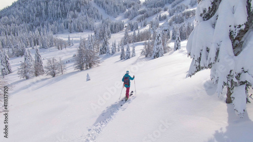 DRONE Flying around active woman on splitboarding trip crossing the snowy meadow