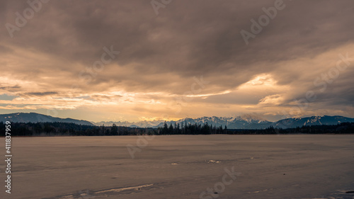 On the shore of the frozen lake Kirchsee with ice sheets in Upper Bavaria with Alps in background in winter with snow