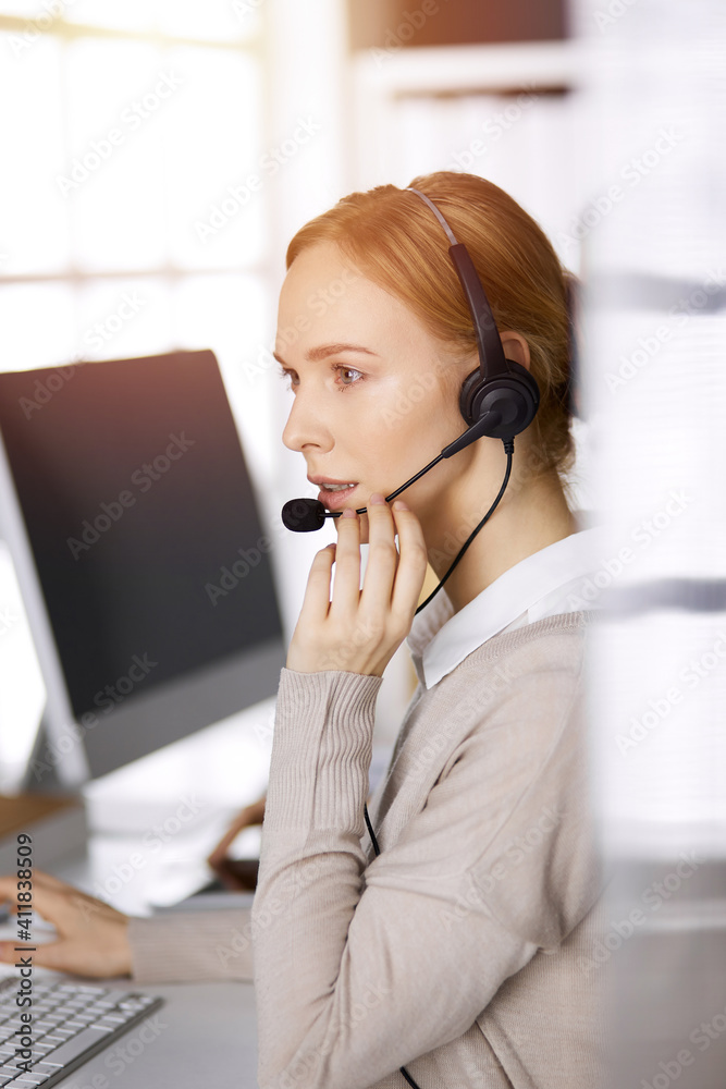 Businesswoman talking by headset while sitting in sunny office. Call center and diverse people group in business Businesswoman talking by headset while sitting in sunny office. Call center and diverse people group in business