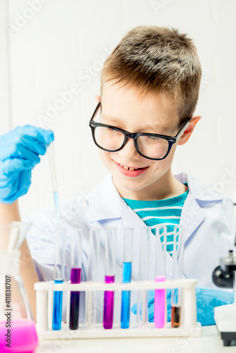 A schoolboy studies multi-colored substances in test tubes  conducts experiments - a portrait on a white background. Concept for the study of coronavirus in the laboratory