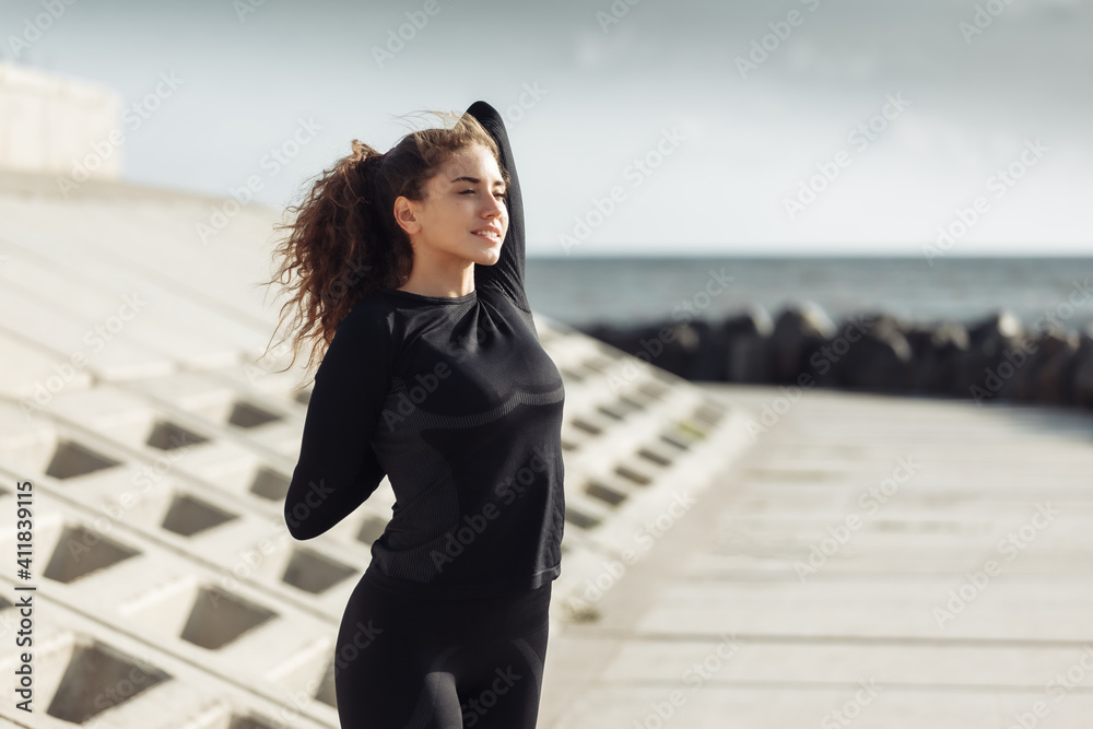 Outdoor workout concept. Fit slim woman with curly hair stretches or warms up on an urban embankment with concrete slabs