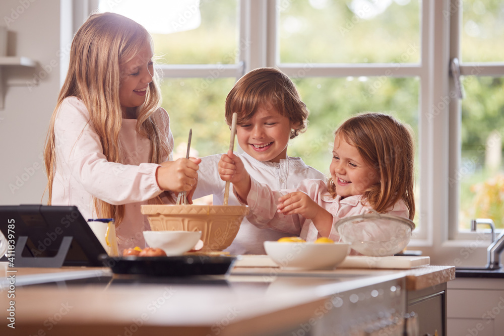 Children In Pyjamas Making Pancakes In Kitchen At Home Following Recipe On Digital Tablet Children In Pyjamas Making Pancakes In Kitchen At Home Following Recipe On Digital Tablet