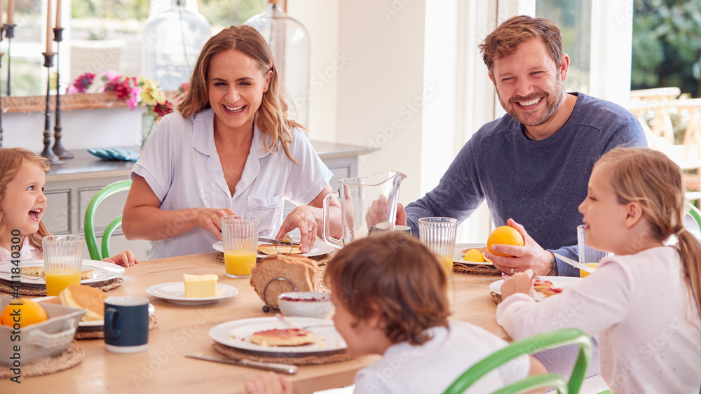 Family Wearing Pyjamas Sitting Around Table Enjoying Pancake Breakfast Together