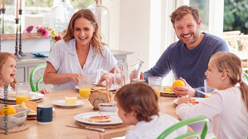 Family Wearing Pyjamas Sitting Around Table Enjoying Pancake Breakfast Together