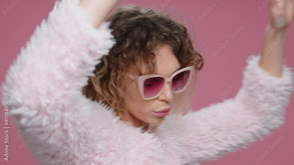 Dancing Happy Young Woman Raises her Hands Up and Moves Rhythmically Music Sings Slow Motion on Pink Background. Portrait Glamorous, Beautiful Girl in sunglasses. Positive Emotions. Freedom. Fashion Dancing Happy Young Woman Raises her Hands Up and Moves Rhythmically Music Sings Slow Motion on Pink Background. Portrait Glamorous, Beautiful Girl in sunglasses. Positive Emotions. Freedom. Fashion