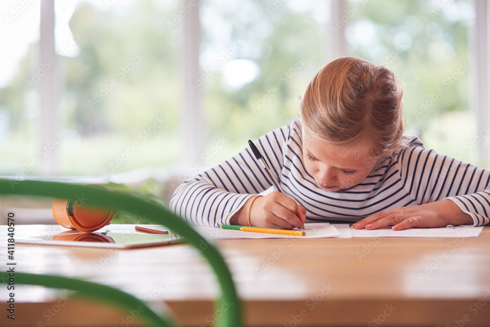 Girl Sitting At Table With Digital Tablet Home Schooling During Health Pandemic Girl Sitting At Table With Digital Tablet Home Schooling During Health Pandemic