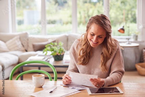 Woman With Digital Tablet Sitting At Table At Home Reviewing Domestic Finances