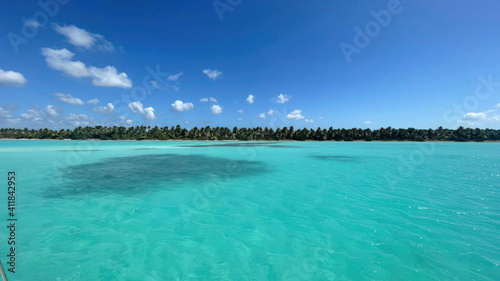 Ocean or sea calm water surface under a blue sky with a few clouds. View on the shore with a beach and tropical trees. Vacation resort paradise in summer time