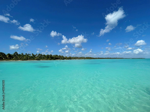 Ocean or sea calm water surface under a blue sky with a few clouds. View on the shore with a beach and tropical trees. Vacation resort paradise in summer time