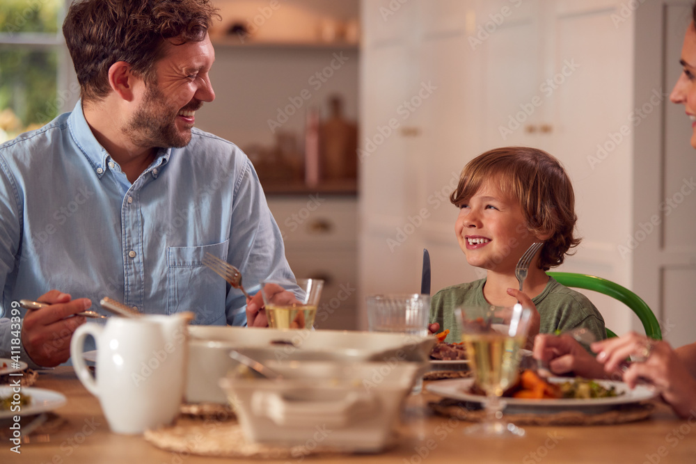 Family Sitting Around Table At Home Enjoying Meal Together Family Sitting Around Table At Home Enjoying Meal Together
