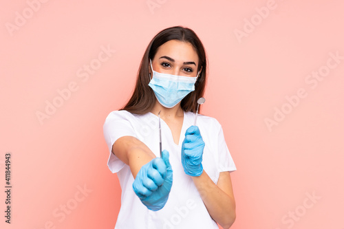 Woman dentist holding tools isolated on pink background