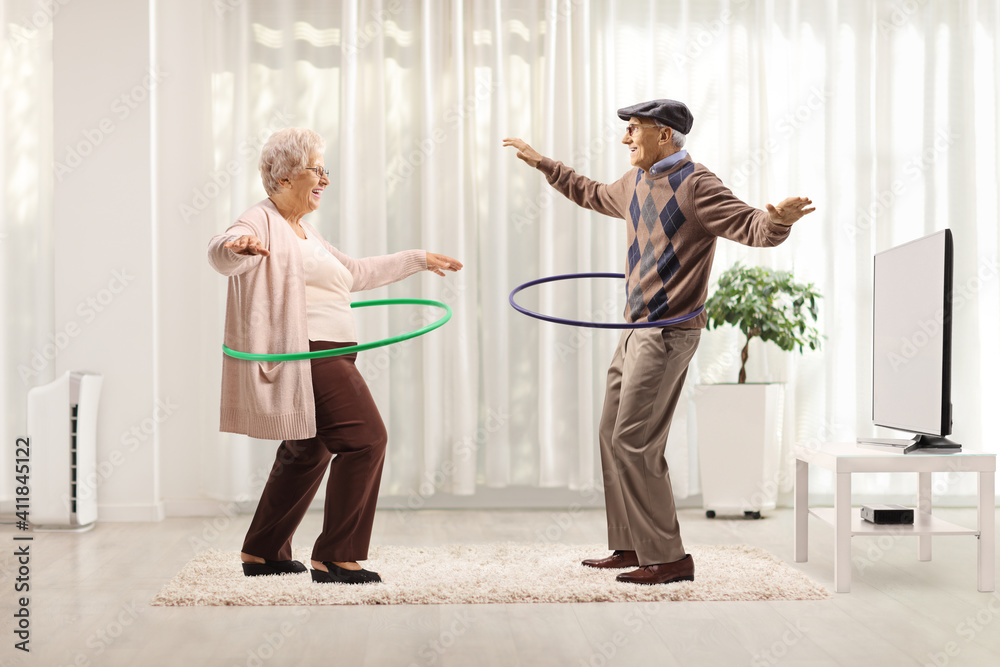 Happy elderly couple spinning hula hoops at home