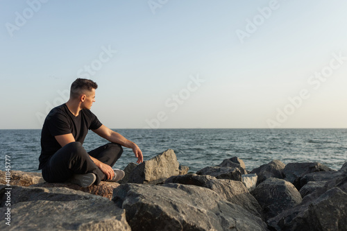 Pensive sports man sits on the coast with stones