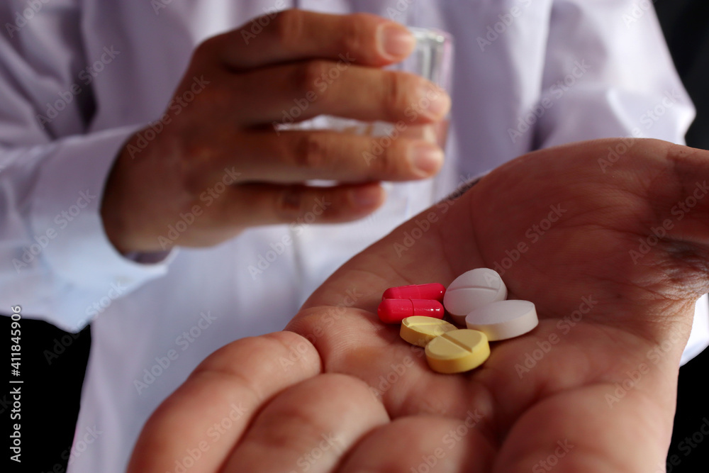 A red, yellow and white pill was placed on the left hand and the right hand held a glass of water to take the pill. A red, yellow and white pill was placed on the left hand and the right hand held a glass of water to take the pill.
