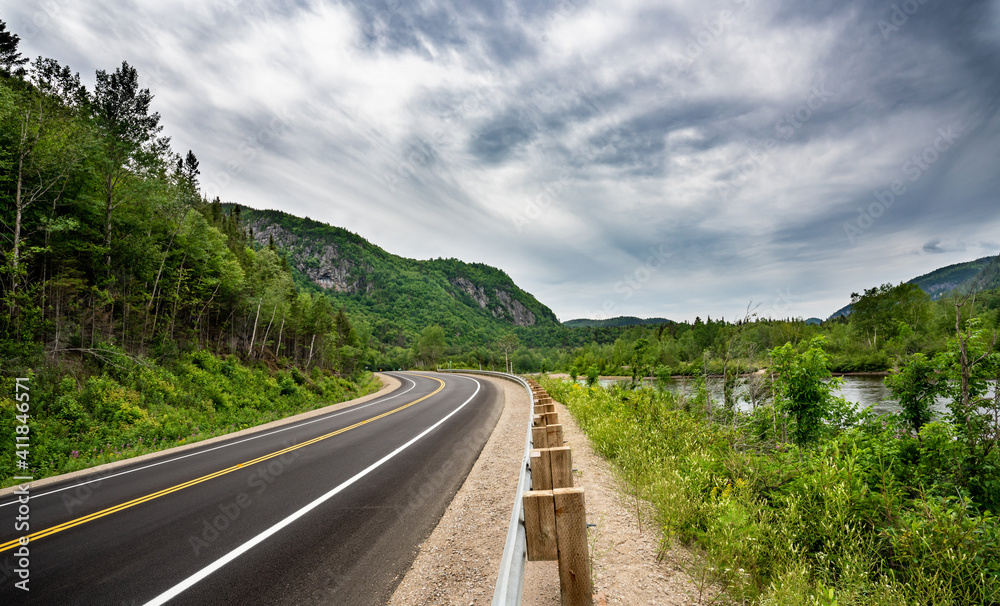 Canadian road in Quebec Province meandering
between river and and cliffs with trees everywhere at summer time during a cloudy day Canadian road in Quebec Province meandering
between river and and cliffs with trees everywhere at summer time during a cloudy day