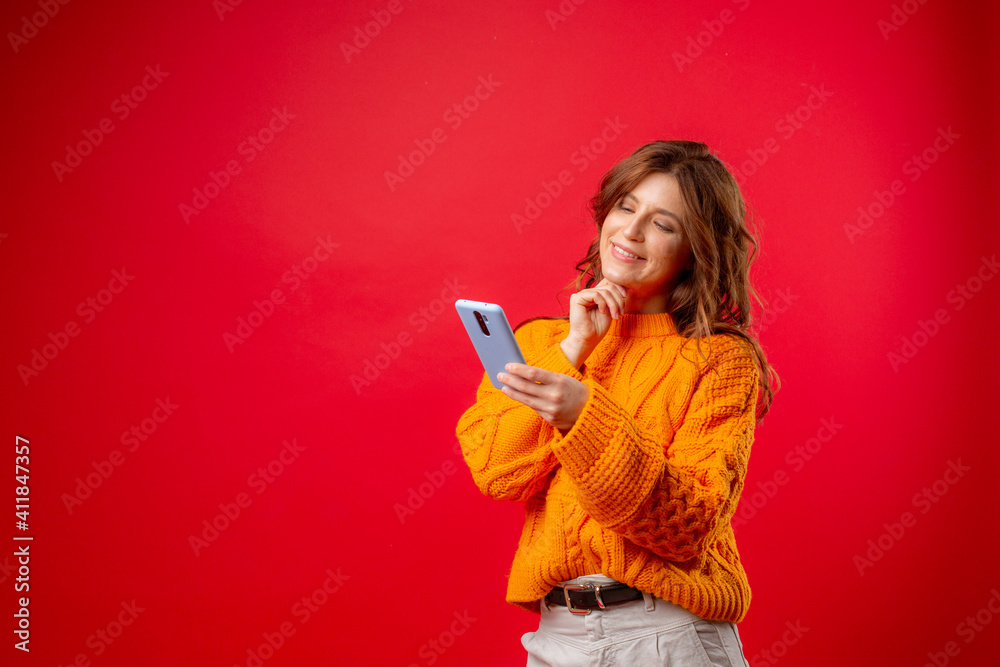 a young woman on a red background is holding a mobile phone typing a message a young woman on a red background is holding a mobile phone typing a message