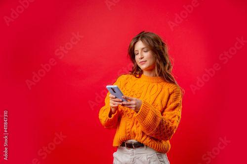 a young woman on a red background is holding a mobile phone typing a message