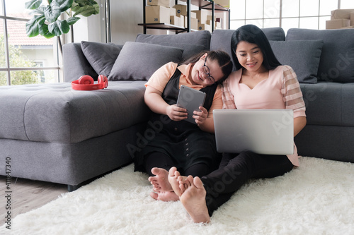  mother with daughter with autism using a laptop and tablet for entertainment and online business in a home converted to a small business office online. 