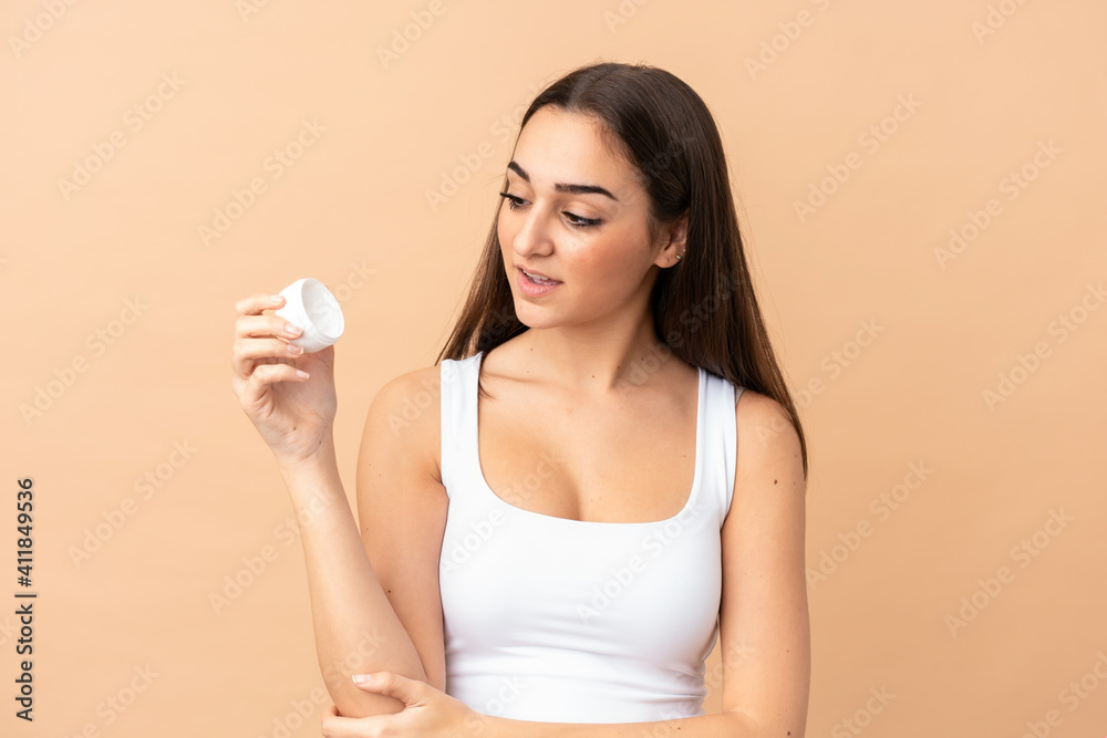 Young caucasian woman isolated on beige background with moisturizer Young caucasian woman isolated on beige background with moisturizer