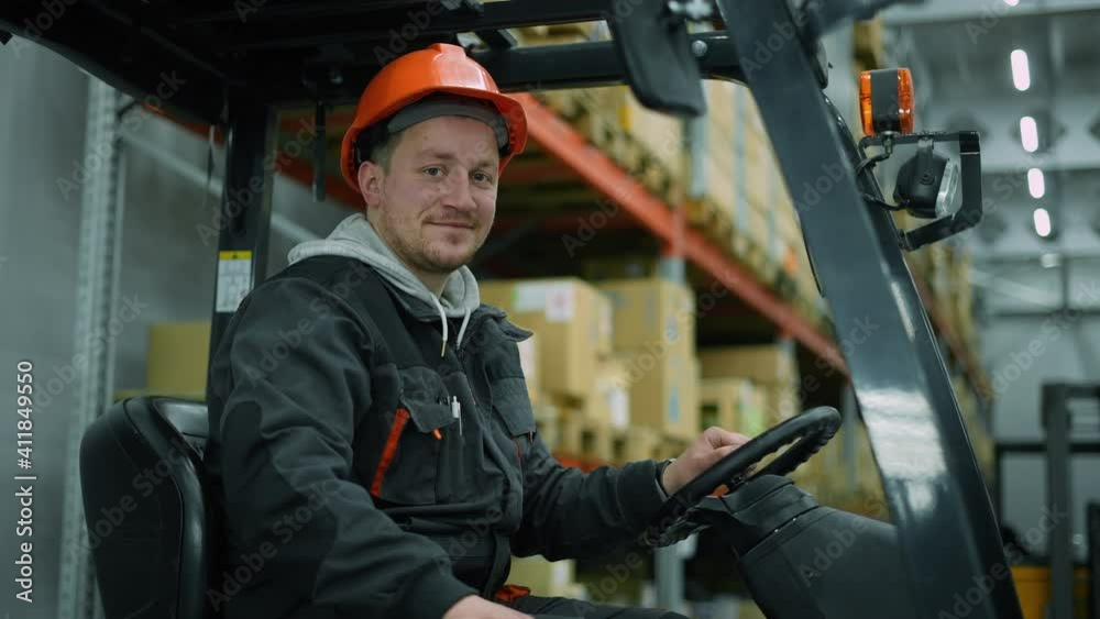The forklift driver smiles for the camera. The action takes place in a warehouse. The forklift driver smiles for the camera. The action takes place in a warehouse.