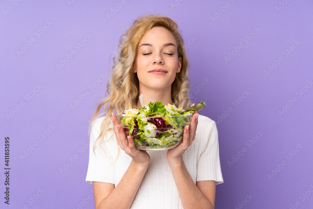 Young blonde woman holding salad isolated on purple background Young blonde woman holding salad isolated on purple background