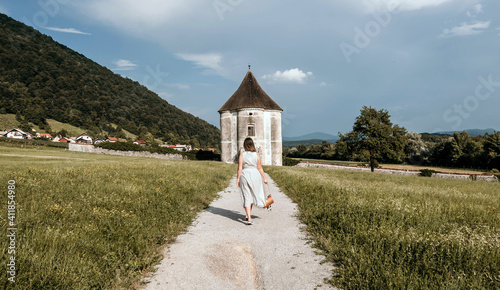 Rear view of woman walking on path leading to old pavilion in green field. photo