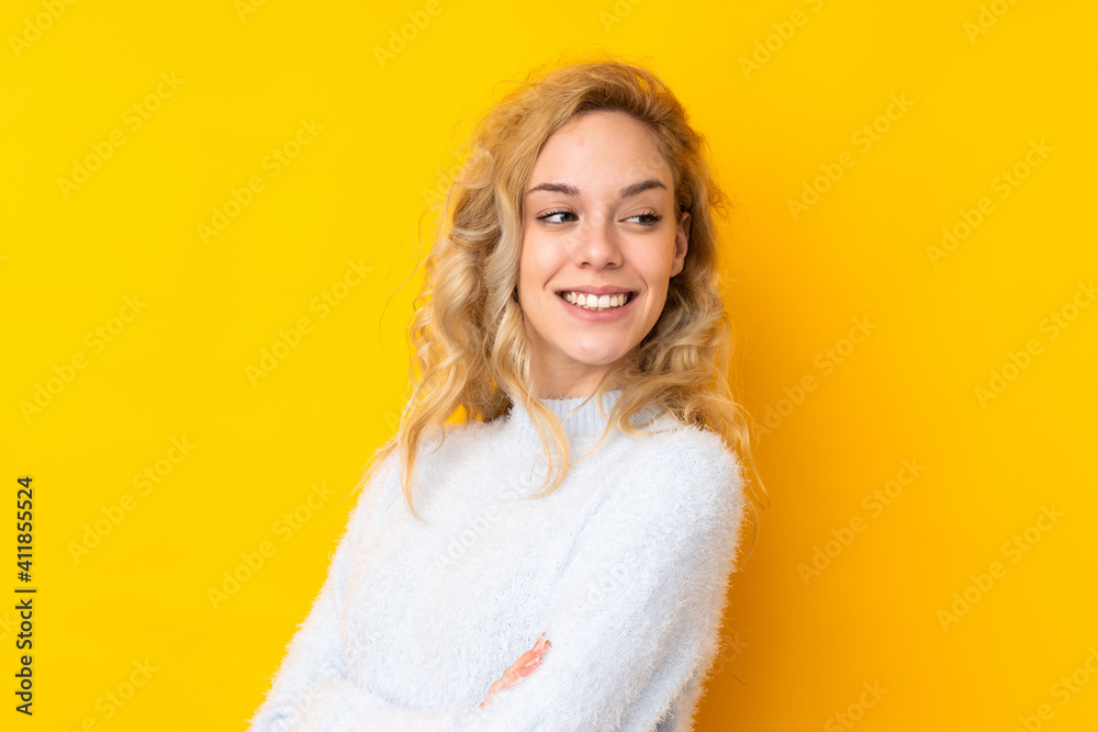 Young blonde woman isolated on yellow background with arms crossed and happy Young blonde woman isolated on yellow background with arms crossed and happy