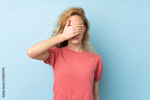 Young blonde woman isolated on blue background covering eyes by hands