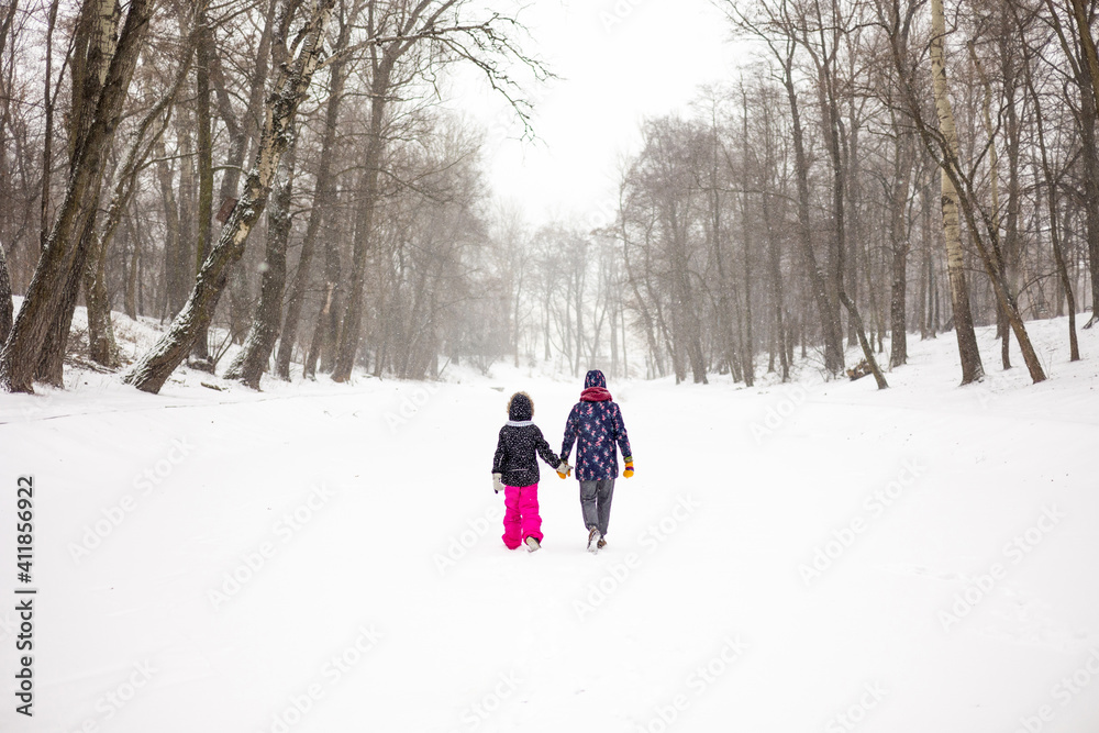 Mother and daughter walking through a winter park

