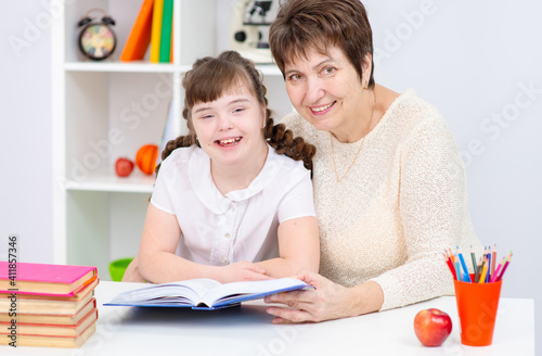 A girl with down syndrome is reading with her mother at home. Education for disabled children concept.
