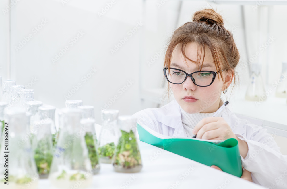 A worker in a biological laboratory fills out a report by examining plants grown in a nutrient solution in flasks. Biological research at the university A worker in a biological laboratory fills out a report by examining plants grown in a nutrient solution in flasks. Biological research at the university