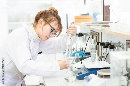 In a chemical laboratory, a girl laboratory assistant drips a solution into a measuring beaker with a special pipette